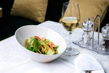 Karidesli salata, salatalık, zeytin, domates ve fesleğen. Bir bardak beyaz şarap. Metin için yer.