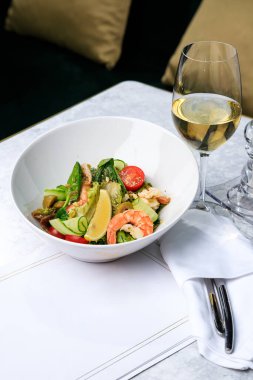 Karidesli salata, salatalık, zeytin, domates ve fesleğen. Bir bardak beyaz şarap. Metin için yer.