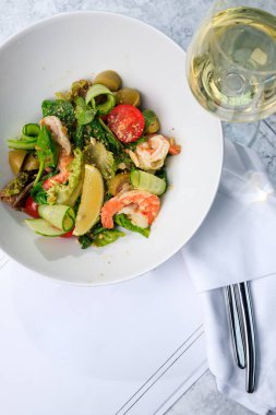 Karidesli salata, salatalık, zeytin, domates ve fesleğen. Bir bardak beyaz şarap. Metin için yer.