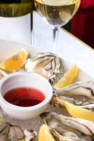 Fresh oysters in a white plate with ice and lemon. Open Oysters and glass of white wine. Tasty Oysters On Ice.