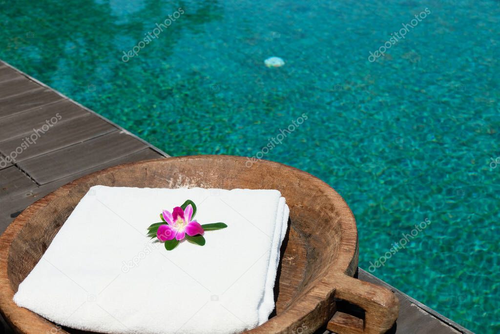 White clean towel with orchid flower decoration beside the pool inside resort and spa. Vacation or travel with nature, relaxation environment concept with copy space for text.
