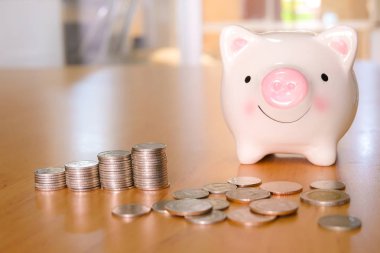 Seçici odak domuz kumbarası bozuk para ile ahşap masa üzerinde doğal ışık arka planı ile doldurulmuş para yığını. Para ve finansal tasarruf, hayat harcama planlama yaşam tarzı zenginlik kavramı.