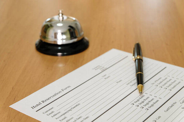 Hotel reservation form and luxury pen at reception concierge desk. With a bell ring for guest to call for a service, attention. Hotel, hospitality business concept.