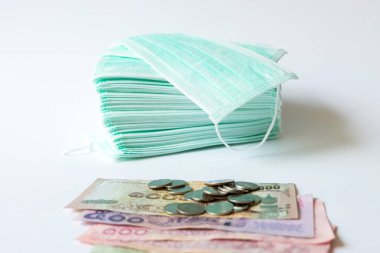 Bir yığın yeşil cerrahi koruyucu yüz maskesi ve izole edilmiş beyaz arka planda para ve para. Çin 'de Corona virüsü salgını sırasında ortaya çıkan kavram, yüz maskesi eksikliği daha yüksek fiyattaki talebi artırır.