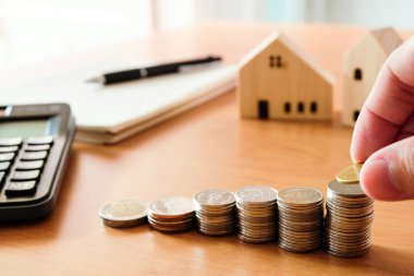 Seçici odak Adamları ev için biriktirdikleri para yığınına para koyuyorlar, arka planda küçük ahşap bir ev olan mülke. Konut kredisi için sermaye ve tasarruf planı. Kişisel yatırım kavramı.