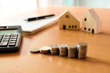 Ev için biriktirmek üzere para yığını, küçük ahşap evi ve arka planda hesap makinesi olan bir mülk seçiniz. Ev kredisi için servet ve tasarruf planı. Kişisel yatırım kavramı.