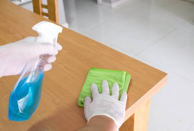 Eldiven takan erkeklerin seçici odak noktası ve alkol dezenfektanı, ahşap masa yüzeyine dezenfektan spreyi. Covid, koronavirüs salgını sırasında aileyi hastalıklardan ve virüsten korumak için çok temiz..