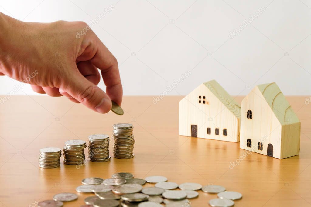 Selective focus Men hand puting coin on stack of money coin for saving for home, property with small wood house on the background. Wealth and saving plan for house mortgage Personal investment concept