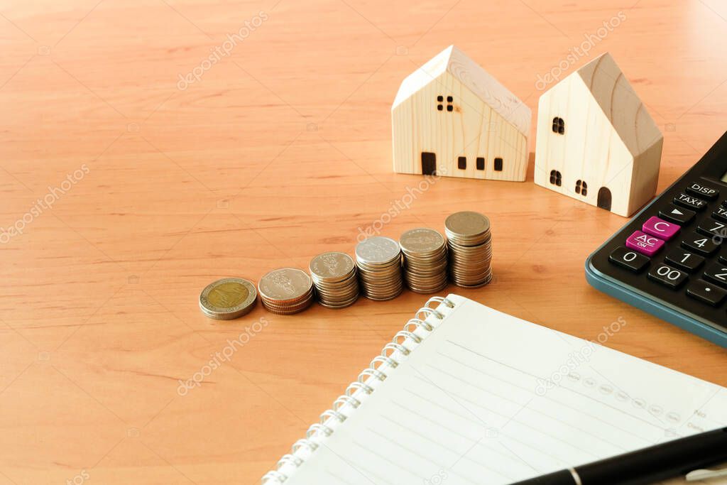 Selectove focus of Stack of money coin for saving for home, property with small wood house and calculator on the background. Wealth and saving plan for house mortgage. Personal investment concept.