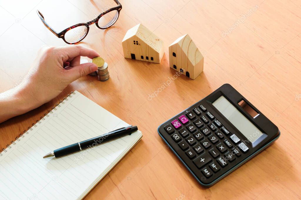 Selective focus Men hand puting coin on stack of money coin for saving for home, property with small wood house on the background. Wealth and saving plan for house mortgage.Personal investment concept