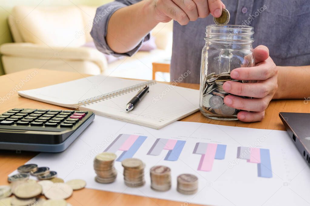 Men sitting in house, put coin into a glass jar and calculate personal saving and expense for future retirement, pension plan. Personal finance concept with calculator coins and infographic graph. 