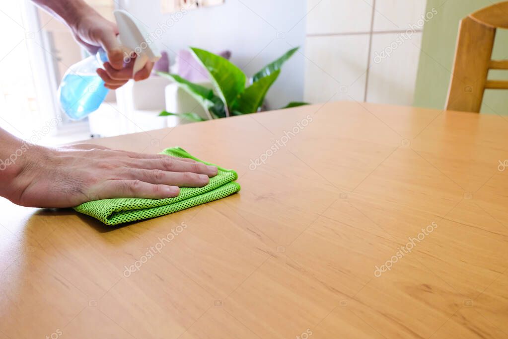 Selective focus of men hand wearing glove and use alcohol sanitizer, disinfectant spray on wood desk surface. Deep clean for protect family from disease and virus during Covid, coronavirus pandemic.