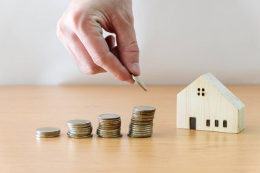 Erkekler kişisel tasarruflarını arttırmak için madeni para koyarlar. Ev kredisi, ev kredisi. Ahşap masa üzerinde küçük ahşap ev ile beyaz arkaplan metin için kopyalama alanı ile. 