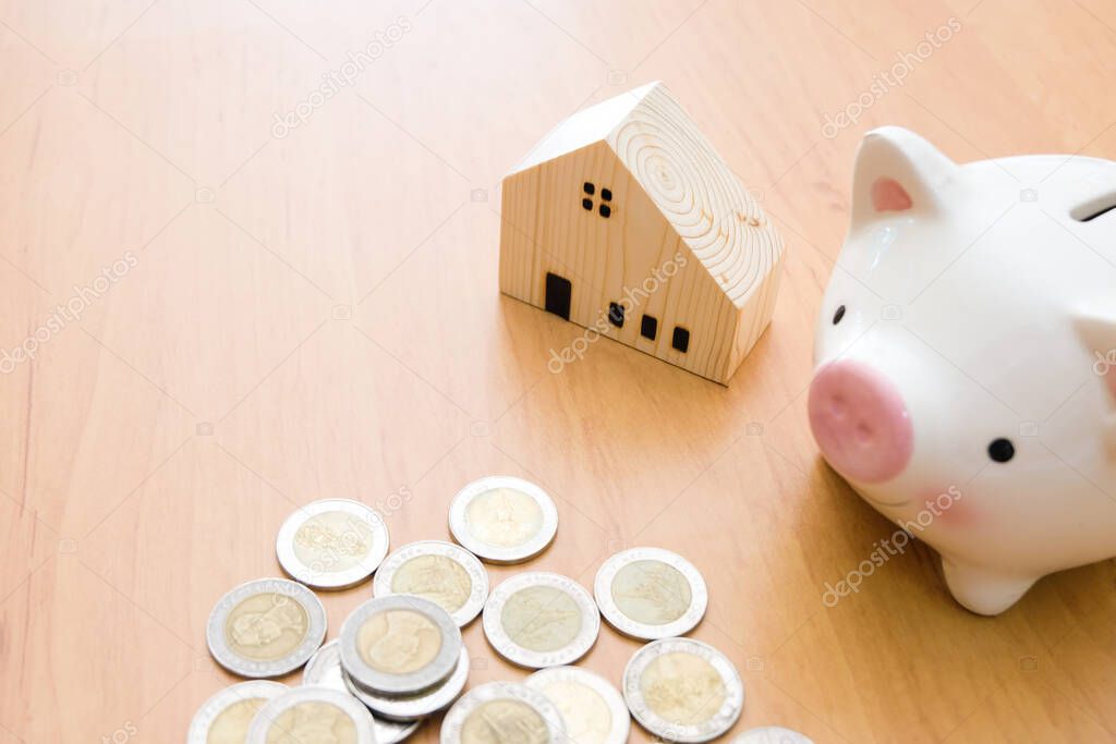 Selective focus of Piggy bank and wooden house on wood table with money coin.Saving plan to buy property, house. Personal financial concept for own a house. with copy space for text