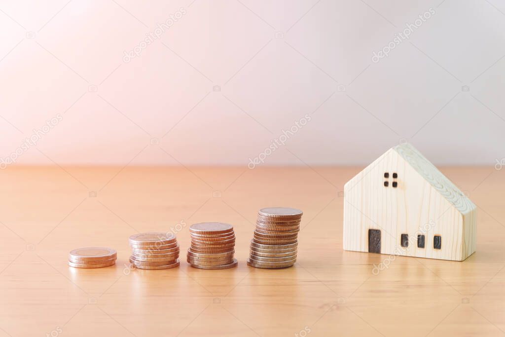 Stack of coin of saving money increasing to reach small wood house on wood table with white background with copy space for text. Personal finance for home or property. Budget planing.