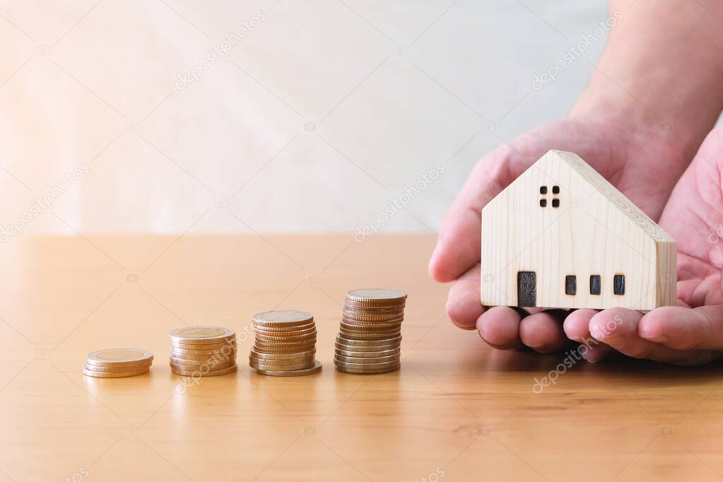 Men hand hold, giving wood house beside increasing money, coin stack on wood table. Saving plan to buy property, house. Personal financial concept for own a house. with copy space for text