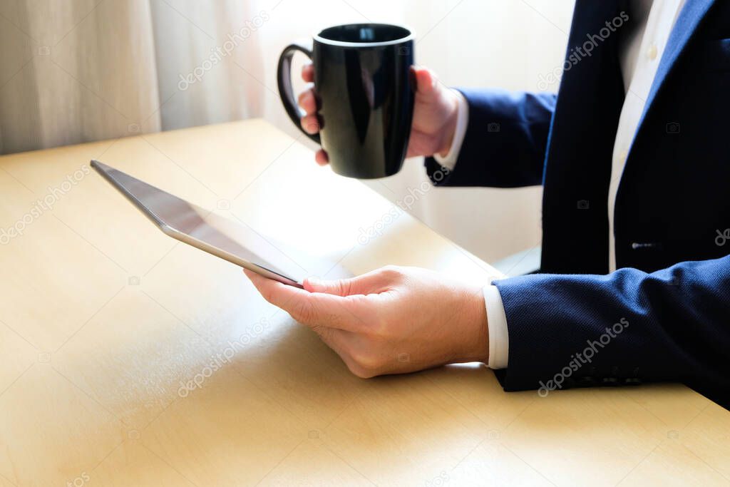 Man business person with suit using tablet device reading news or check for financial stock exchange information while drinking coffee in the morning at the cafe or office. with copy space for text
