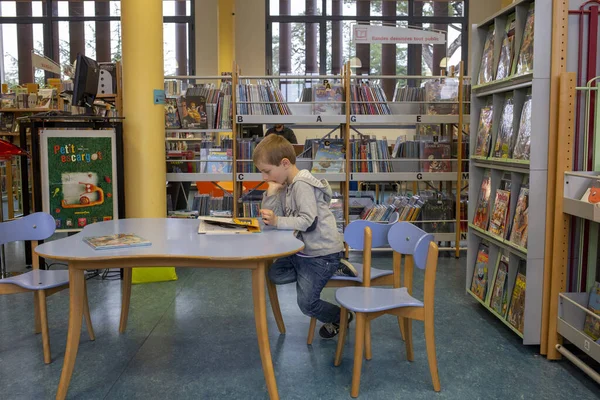 Niño en la biblioteca, libro de lectura, asientos en la mesa —  Fotos de Stock