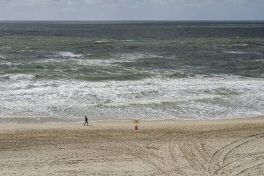 Wenningstedt Plajı 'nda taze rüzgarda yalnız bir sahil yürüyüşçüsü
