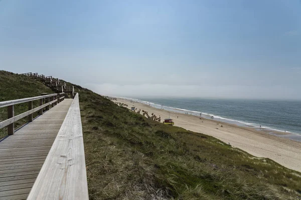 Sylt - Almanya 'nın kuzeyinde Schleswig-Holstein eyâletinde, Wenningstedt' teki Grass Dunes ve Beach 'e doğru tahta kaldırım manzarası