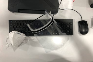 Ofisteki Covid-19 için yüz maskesi ve yüz maskesi, bilgisayar masası, klavye ve fare, beyaz masa.