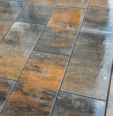 Yağmurdan sırılsıklam olmuş turuncu siyah döşeme levhaları.