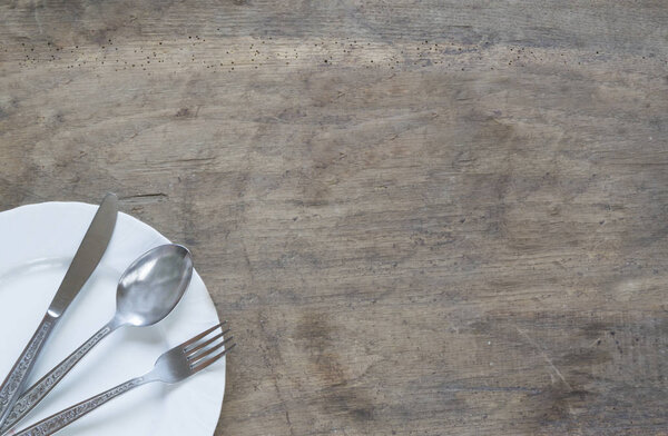 Серебряная ложка, вилка и нож в тарелке на старом ржавом деревянном фоне
