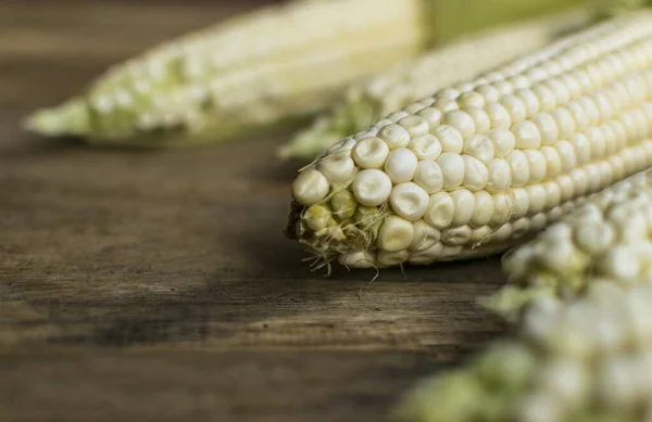 Fresh white corn cobs on old wooden background with place for text . Selective focus