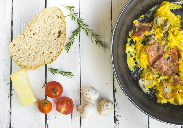 Beyaz masada pastırmalı ve mantarlı omlet. Süs olarak vişneli domates, peynir ve biberiye. Yüksek açı görünümü