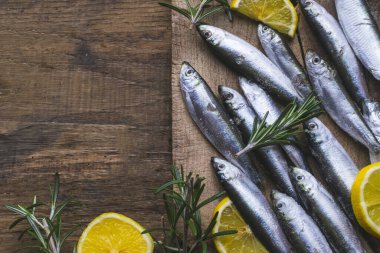 Eski, koyu, ahşap masada limon ve biberiyeli taze donmuş sardalya. Kopyalama alanı ile yüksek açı görünümü