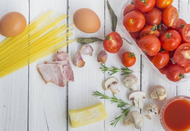 Beyaz arka planda makarna pişirmek için çeşitli malzemeler ve spagetti ile çerçevelenmiş..