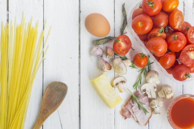 Beyaz arka planda makarna pişirmek için çeşitli malzemeler ve spagetti ile çerçevelenmiş..