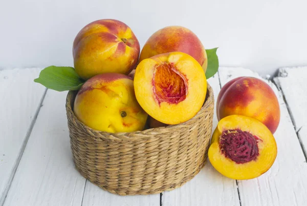 Delicious and juicy peach (nectarina) in basket  on white wooden table with place for text