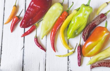 Eski beyaz ahşap masa üzerinde çeşitli renkli ve taze biber (paprika) türleri. Yüksek açı görünümü