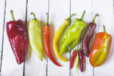 Eski beyaz ahşap masa üzerinde çeşitli renkli ve taze biber (paprika) türleri. Yüksek açı görünümü