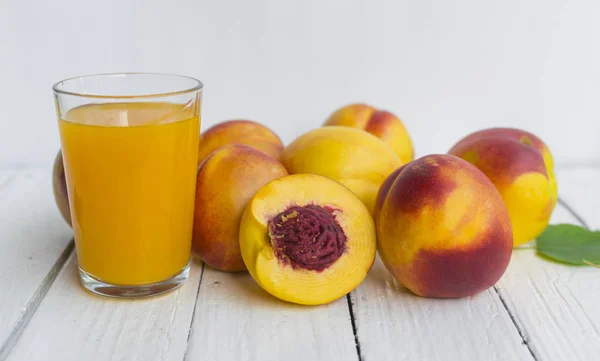 Delicious and juicy peach (nectarina) with glass of juice on white wooden table.