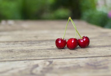 Eski ahşap masada üç taze ve lezzetli kiraz..