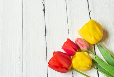 Eski beyaz ahşap masada taze kırmızı ve sarı laleler.