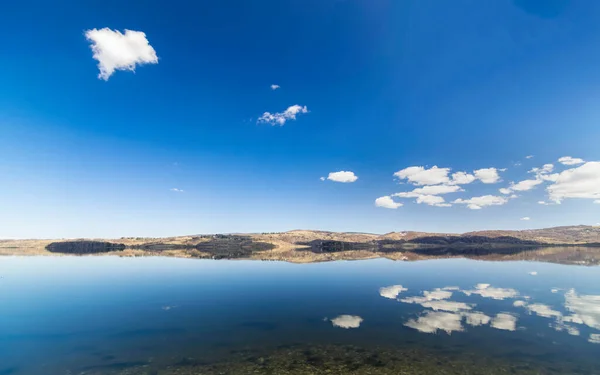 Baharın başlarında Sırbistan 'ın güneyindeki Vlasina gölünün panoramik manzarası. Sakin sulardaki bulutların yansıması