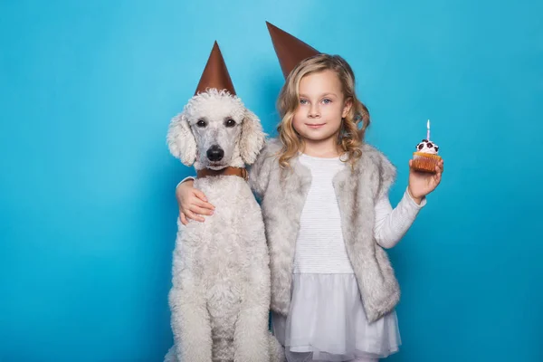 Маленькая красивая девочка с собакой празднует день рождения. Дружба. С любовью. Торт со свечой. Студийный портрет на синем фоне — стоковое фото
