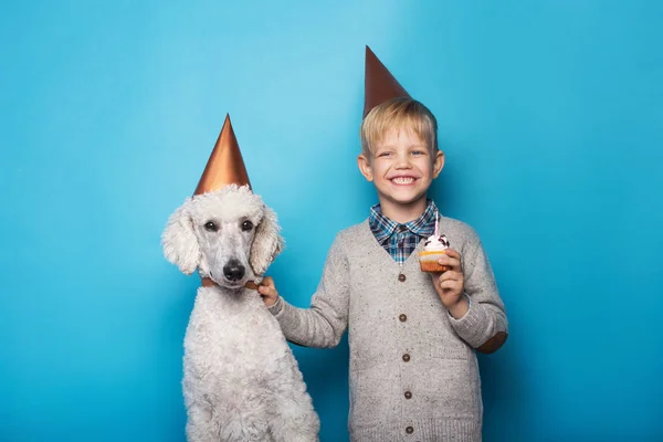 Маленький красивый мальчик с собакой празднует день рождения. Дружба. С любовью. Торт со свечой. Студийный портрет на синем фоне — стоковое фото