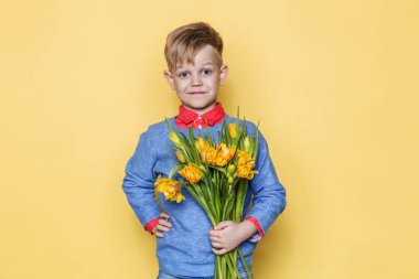 Lale bir buket ile küçük güzel çocuk. Oğlu anne çiçek kadınlar günü, anneler günü verir. Doğum günü. Sevgililer günü. Bahar. Stüdyo portre sarı arka plan üzerinde