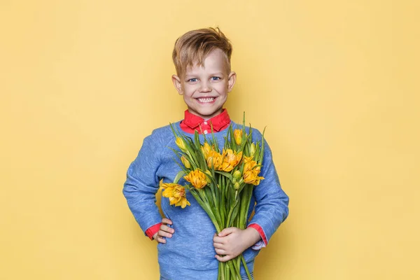 Petit bel enfant avec un bouquet de tulipes. Le fils donne des fleurs à maman le jour de la fête des mères. Anniversaire. Saint-Valentin. Le printemps. Portrait studio sur fond jaune — Photo