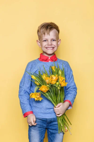 Little beautiful child with a bouquet of tulips. Son gives mom flowers on Women\'s Day, Mother\'s Day. Birthday. Valentine\'s day. Spring. Studio portrait over yellow background