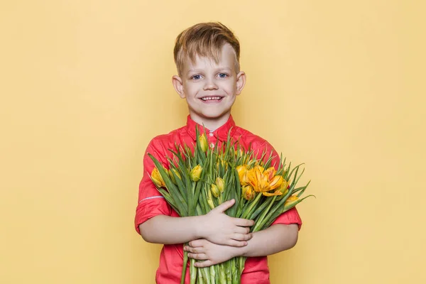 Pequena criança bonita com camisa rosa dá um buquê de tulipas no Dia das Mulheres, Dia das Mães. Aniversário. Dia dos Namorados. Primavera. Retrato de estúdio sobre fundo amarelo — Fotografia de Stock