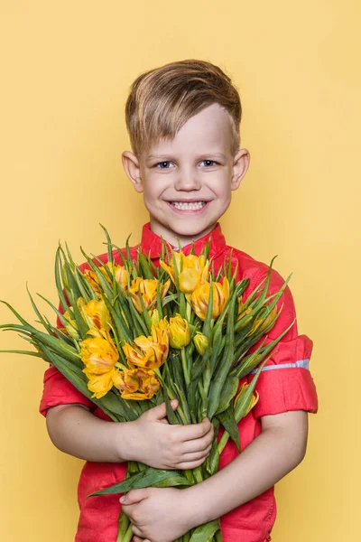 Little beautiful child with pink shirt gives a bouquet of tulips on Women's Day, Mother's Day. Birthday. Valentine's day. Spring. Studio portrait over yellow background