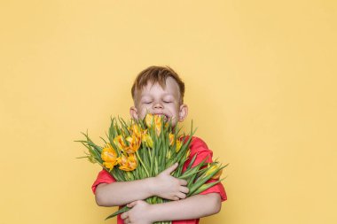 Pembe gömlek ile küçük güzel çocuk, kadınlar günü, anneler günü için bir buket çiçek verir. Doğum günü. Sevgililer günü. Bahar. Yaz. Stüdyo portre sarı arka plan üzerinde