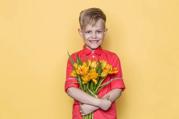 Pequena criança bonita com camisa rosa dá um buquê de flores no Dia das Mulheres, Dia das Mães. Aniversário. Dia dos Namorados. Primavera. Verão. Retrato de estúdio sobre fundo amarelo — Fotografia de Stock