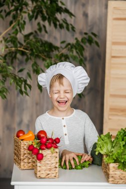 Yakışıklı çocuk aşçı sebze ile üniforma içinde. Evde mutfak yemek. Vejetaryen. Sağlıklı gıda