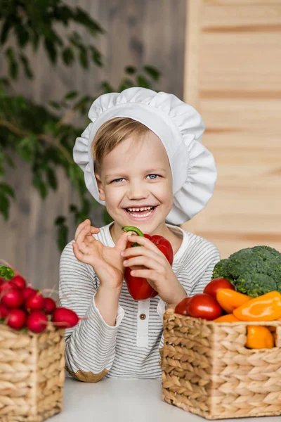 Lindo chico en uniforme de chef con verduras. Cocinar en la cocina en casa. Vegetariano. Alimento saludable — Foto de Stock